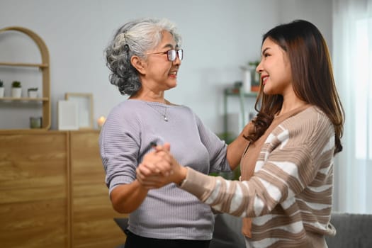 Smiling elderly mother and adult daughter dancing and spending leisure weekend time together at home.