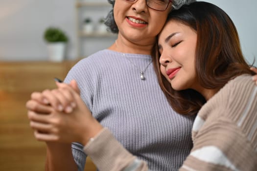 Loving young adult female and senior mother holding hand and hugging together with love.