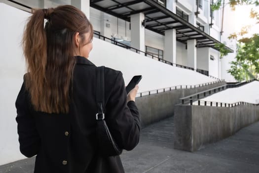 Attractive smiling Asian businesswoman wearing a suit standing in the city using an application on her mobile phone Read news on your smartphone fast connection Check out the outdoor mobile app.