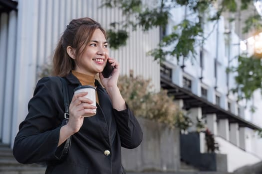 Asian businesswoman talking on mobile phone and holding coffee cup Businesswoman holding a paper cup and calling on a smartphone outside the office.