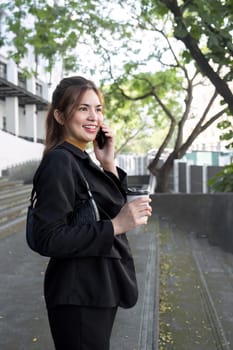 Asian businesswoman smiling while talking on mobile phone and holding coffee cup.