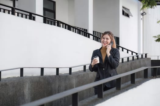 Asian businesswoman talking on mobile phone and holding coffee cup Businesswoman holding a paper cup and calling on a smartphone outside the office.