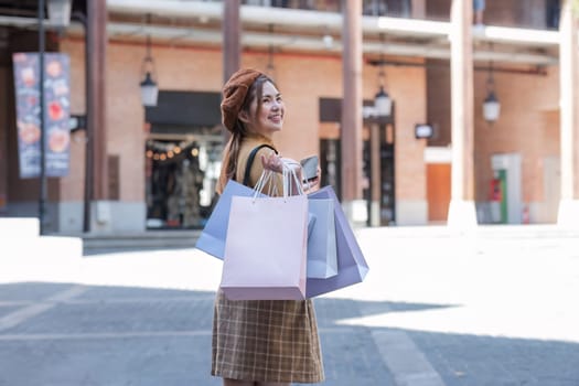 Beautiful Asian woman holding shopping bags and smiling while shopping at the shopping center on the weekend or Black Friday outside the shopping mall..