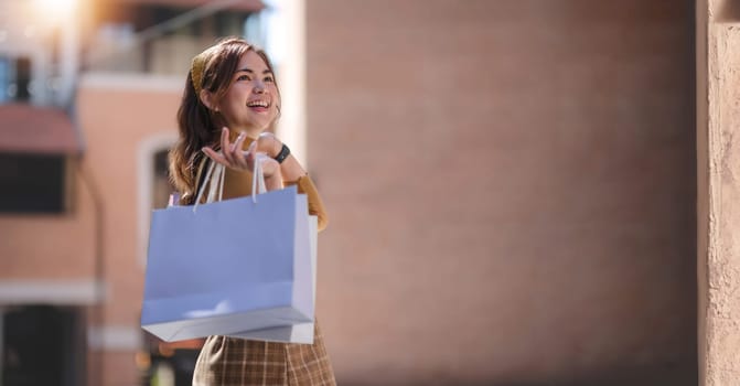 Beautiful Asian woman holding shopping bags and smiling while shopping on Black Friday outside the mall.