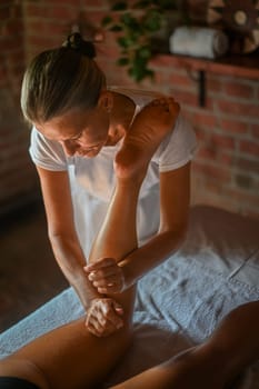 professional caucasian female physiotherapist masseuse performing leg massage to hispanic latino brunette woman in spa clinic