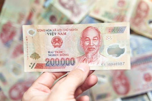 Male hand holds a fan of Vietnames Dong banknote, the currency of Vietnam. Close up Polymer Money of Vietnam. 200000 Dong or VND in male hand. In front a portrait of Ho Chi Minh. Plastic banknotes. High quality photo