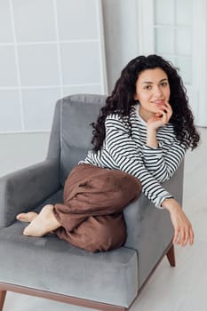 Beautiful oriental brunette woman sitting on grey armchair