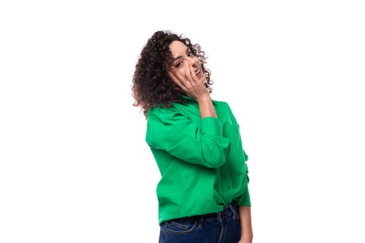 young positive caucasian lady with black curls is dressed in a green shirt in the studio.
