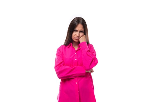 sad young brunette european woman in a crimson shirt on a white background with copy space.