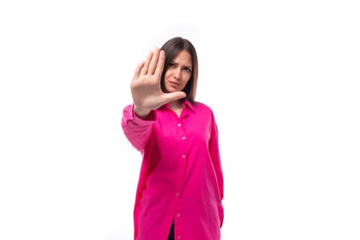 pretty young brunette woman in a bright pink shirt has doubts on a white background with copy space.