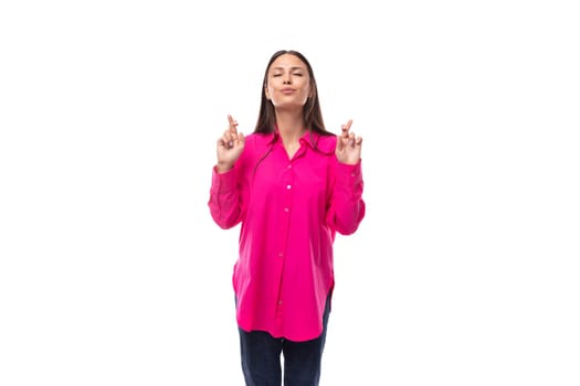 stylish charming young brunette in a bright pink shirt crossed her arms in hope on a white background with copy space.