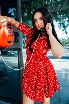 brunette talking on the phone in a booth on the street