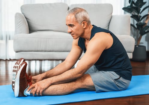 Active and fit senior man warmup and stretching before home exercising routine at living room. Healthy fitness lifestyle concept after retirement for pensioner. Clout