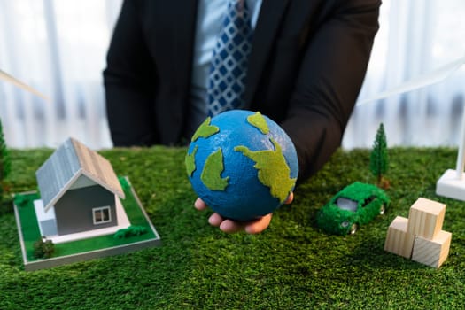 Eco business and save Earth concept shown by businessman or CEO holding paper globe in office with eco friendly mockup to promote CO2 and carbon footprint reduction for greener future. Quaint