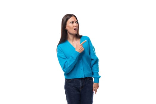 young pleasantly surprised pretty european brunette woman dressed in a blue button-down sweater rejoices on a white background with copy space.