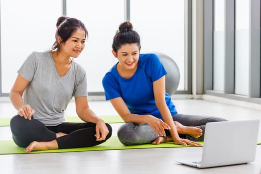 Overhead two Asian lifestyle adult and young woman in sportswear sitting floor on mat look laptop computer for training videos online in yoga studio, fit sport healthy workout exercise