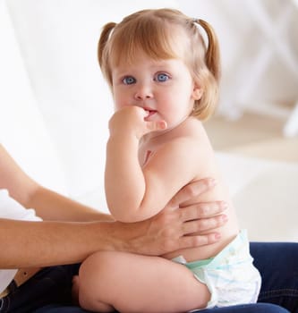 Portrait, family and a girl baby on the lap of a parent closeup on the floor of a living room in their home. Kids, growth and child development with hands holding a cute young toddler in a diaper.