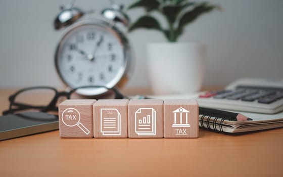 Wooden block printed tax symbols icons placed on a wooden tabletop with office supplies, financial research, reports, tax return calculations.