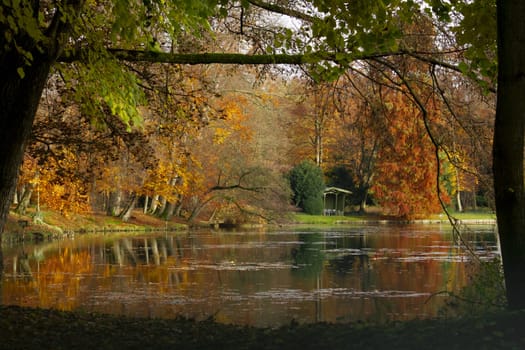 Picturesque autumn scenery with gazebo on the lake shore and colorful trees. High quality photo