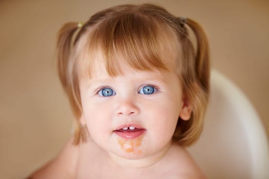 Portrait, eating and a girl baby with food on her face closeup in the home for growth or child development. Kids, breakfast and adorable little infant in a feeding chair for health, diet or nutrition.