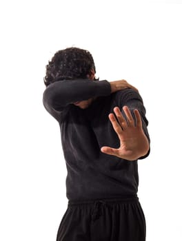 A scared man in a black sweater is protecting himself with one arm and making a stop sign with the other hand, in studio on white