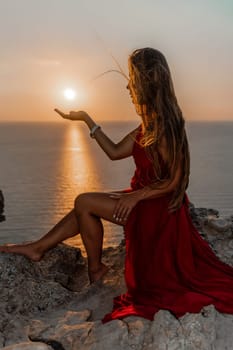 Woman sunset sea red dress, side view a happy beautiful sensual woman in a red long dress posing on a rock high above the sea on sunset