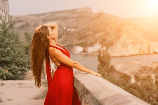 Woman red dress. Summer lifestyle of a happy woman posing near a fence with balusters over the sea