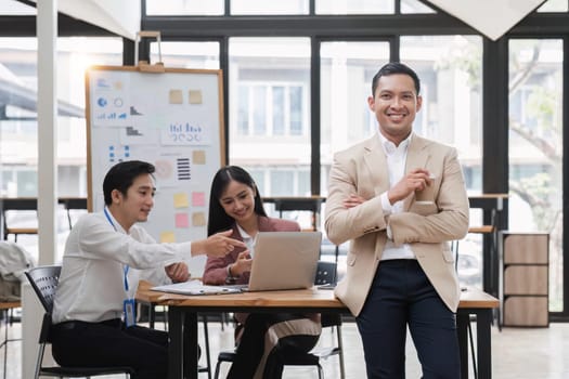 Portrait of a young businessman standing in an office where employees are working..