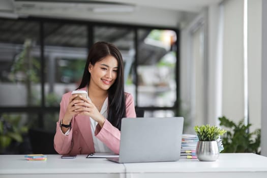 Businesswoman working with laptop computer while having a leisurely cup of coffee at the office in the morning..