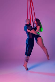 Gymnasts performance on a red canvases. Beautiful girl and an athletic man in a dark sport suits are doing acrobatic elements in a studio against a colorful background. Dancing in the air with balance.