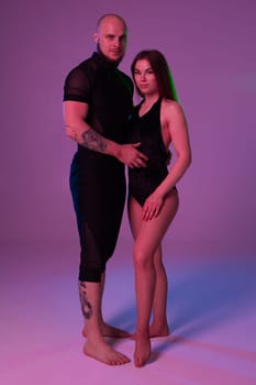 Cute woman and an athletic male in a dark sport suits are looking at the camera while posing in a studio against a colorful background. Gymnasts performance.