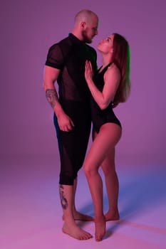 Lovely girl and an athletic man in a dark sport suits are looking at each other while posing in a studio against a colorful background. Gymnasts performance.