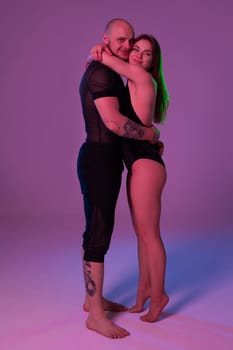 Attractive lady and an athletic fellow in a dark sport suits are hugging each other while posing in a studio against a colorful background. Gymnasts performance.