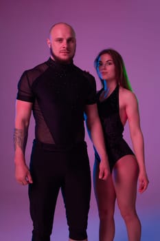 Charming woman and an athletic male in a dark sport suits are looking at the camera and posing in a studio against a colorful background. Gymnasts performance.