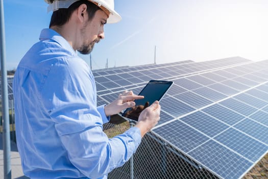 Engineer working with a tablet with photovoltaic solar panel system plant in the background. Green clean energy concept.