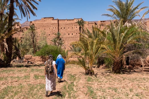 Farmland in front of the scenic berber village Tamenougalt in the Draa valley, a tourist being led by a berber to the village, Morocco