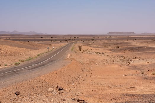 A road leading through the desert near Merzouga, famous horseshoe mountain Gara Medouar in the background, Morocco