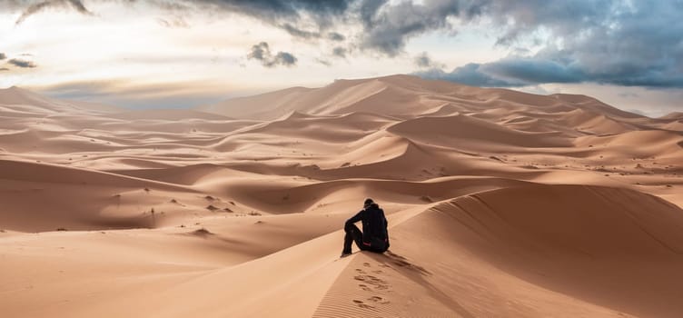 A person sitting in the Erg Chebbi desert in the African Sahara, Morocco