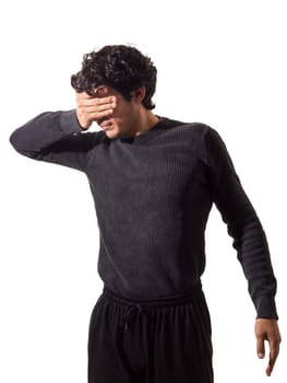 A young man wearing a black sweater and black pants covering eyes with his hand, not wanting to see