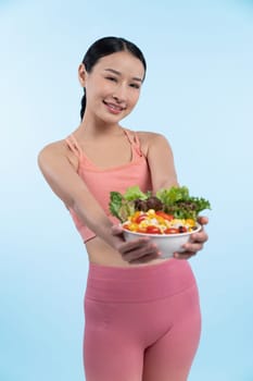 Young sporty Asian woman in sportswear holding salad bowl fill with vibrant of fruit and vegetable. Natural youthful and fit body lifestyle with balance nutrition on isolated background. Vigorous