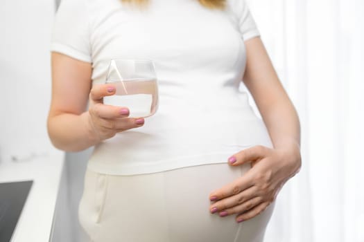 Close up glass of water in pregnant womans hand. Diet during pregnancy.