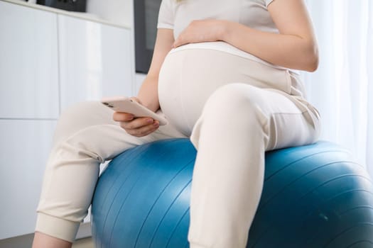 Pregnant woman uses a mobile phone while sitting on the fit ball.