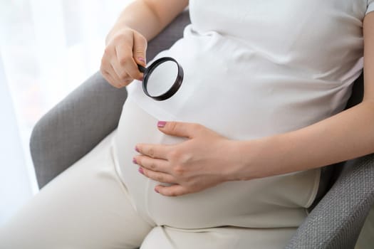 Close up magnifying glass near her belly of pregnant woman.