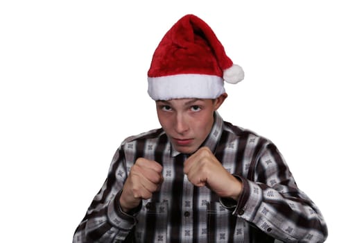 A boy in a Santa hat looks at the camera. Cute, Teenager boy in a shirt, wearing a Santa Claus hat, holding his fists and looking at the camera, on a white isolated background.