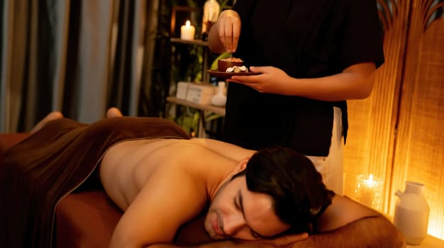 Man customer having exfoliation treatment in luxury spa salon with warmth candle light ambient. Salt scrub beauty treatment in Health spa body scrub. Quiescent