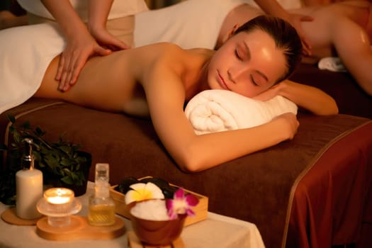 Caucasian couple customer enjoying relaxing anti-stress spa massage and pampering with beauty skin recreation leisure in warm candle lighting ambient salon spa at luxury resort or hotel. Quiescent