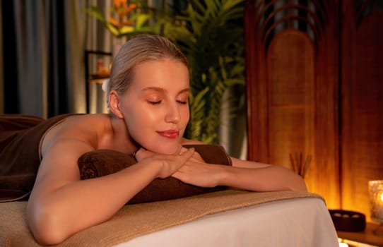 Caucasian woman customer enjoying relaxing anti-stress spa massage and pampering with beauty skin recreation leisure in warm candle lighting ambient salon spa at luxury resort or hotel. Quiescent