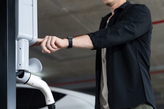 Young man travel with EV electric car to shopping center parking lot charging in downtown city showing urban sustainability lifestyle by green clean rechargeable energy of electric vehicle innards