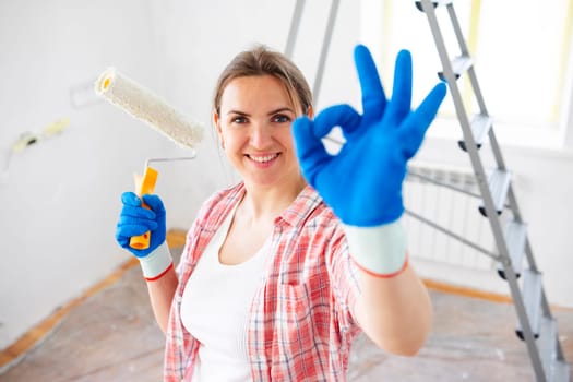 Young smiling woman with roller brush showing ok gesture. Renovation, repair and redecoration concept
