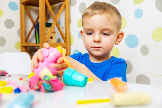 Little boy enthusiastically plays with plasticine, play dough on white table at home, children's creativity concept. Development of fine motor skills